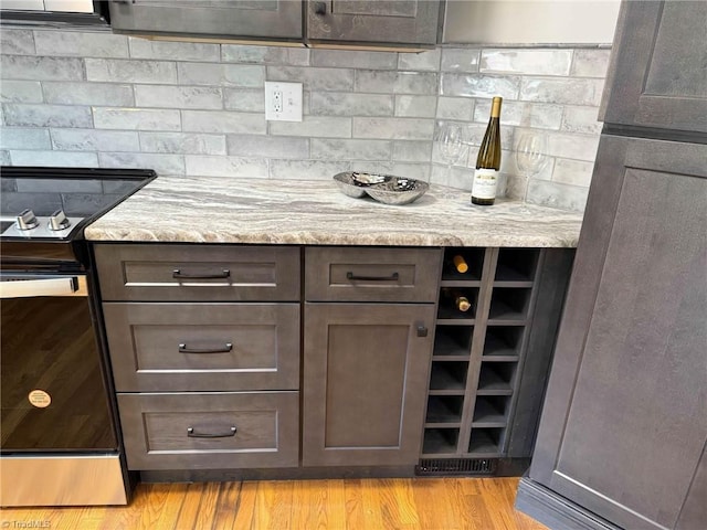 kitchen featuring electric range oven, light stone counters, decorative backsplash, and light wood-type flooring