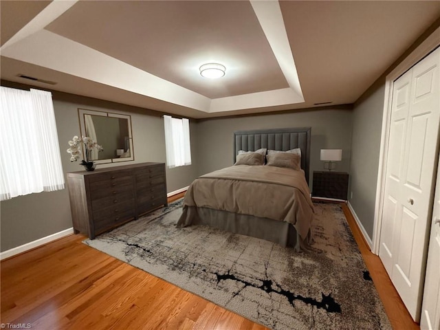 bedroom featuring a tray ceiling, baseboards, and wood finished floors