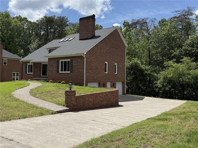 view of property exterior with a chimney, brick siding, an attached garage, and driveway