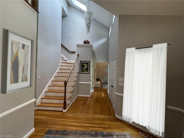 entryway with wood finished floors, high vaulted ceiling, baseboards, and stairs
