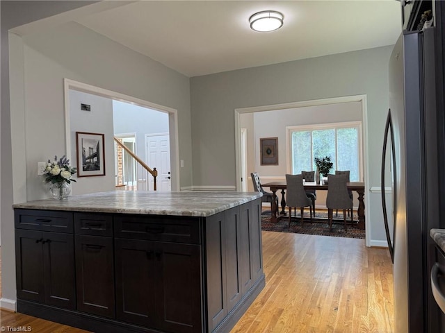 kitchen with freestanding refrigerator, a peninsula, light wood-style flooring, light stone countertops, and baseboards