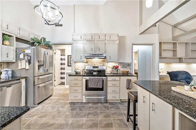 kitchen featuring a high ceiling, hanging light fixtures, decorative backsplash, stainless steel appliances, and a chandelier