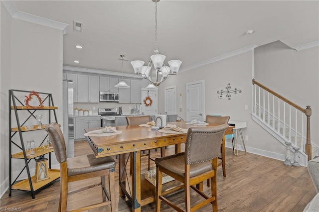 dining area featuring crown molding, sink, light hardwood / wood-style floors, and a notable chandelier