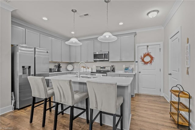 kitchen featuring pendant lighting, sink, crown molding, appliances with stainless steel finishes, and a kitchen island with sink