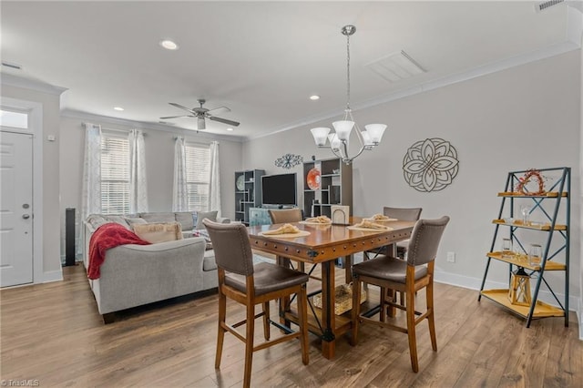 dining area featuring wood-type flooring, ornamental molding, and ceiling fan with notable chandelier