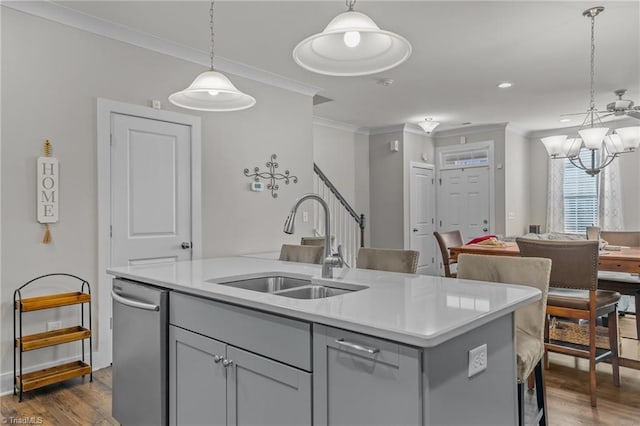 kitchen with sink, hanging light fixtures, stainless steel dishwasher, ornamental molding, and a kitchen island with sink