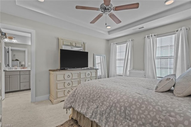 carpeted bedroom with ensuite bathroom, ceiling fan, and a tray ceiling