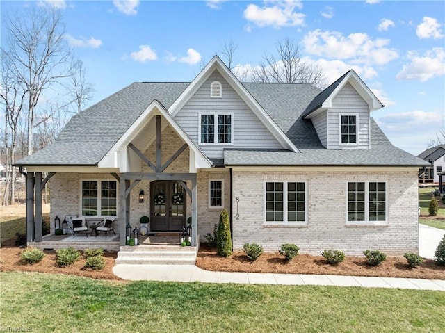 view of front facade featuring brick siding, roof with shingles, a front lawn, and french doors