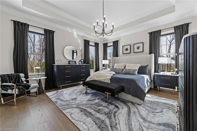 bedroom featuring an inviting chandelier, crown molding, a raised ceiling, and wood finished floors