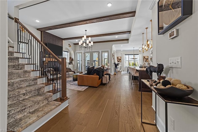 living area featuring stairway, hardwood / wood-style floors, an inviting chandelier, french doors, and beam ceiling