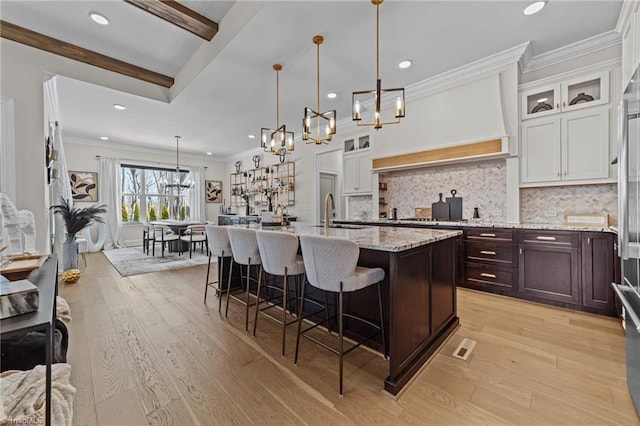 kitchen featuring white cabinetry, a kitchen breakfast bar, light stone countertops, tasteful backsplash, and a center island with sink