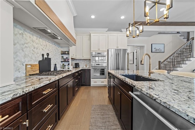 kitchen with a notable chandelier, a sink, white cabinets, appliances with stainless steel finishes, and crown molding