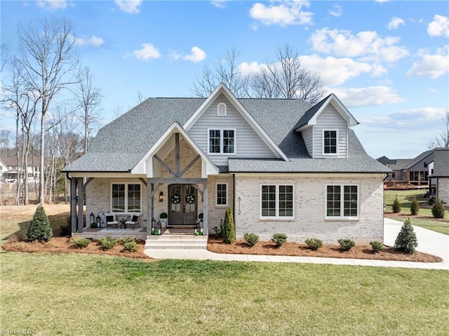 view of front of property with french doors, a front yard, brick siding, and a shingled roof