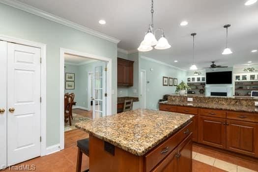 kitchen with ceiling fan with notable chandelier, decorative light fixtures, a center island, and light stone countertops