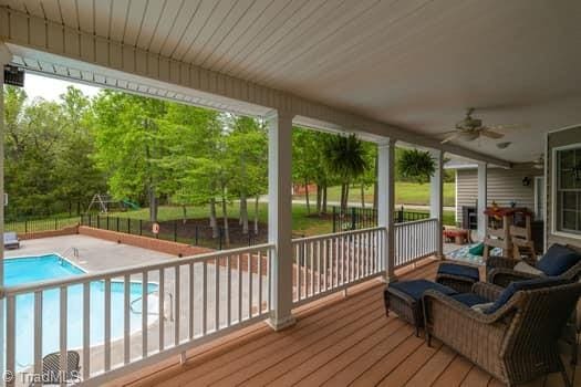 wooden terrace featuring a patio area, ceiling fan, and a fenced in pool