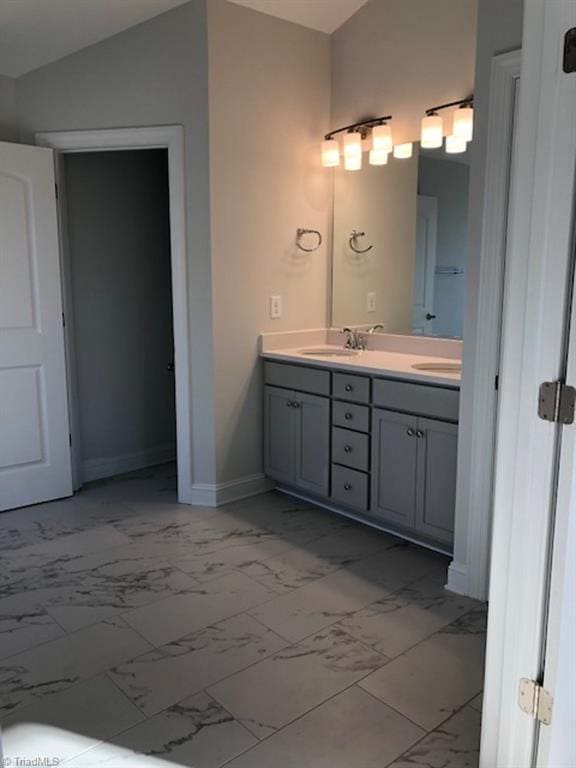 full bath featuring double vanity, marble finish floor, baseboards, and lofted ceiling