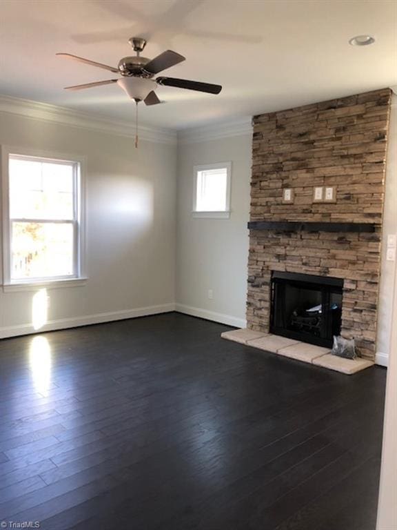 unfurnished living room featuring baseboards, a stone fireplace, dark wood-style floors, crown molding, and ceiling fan