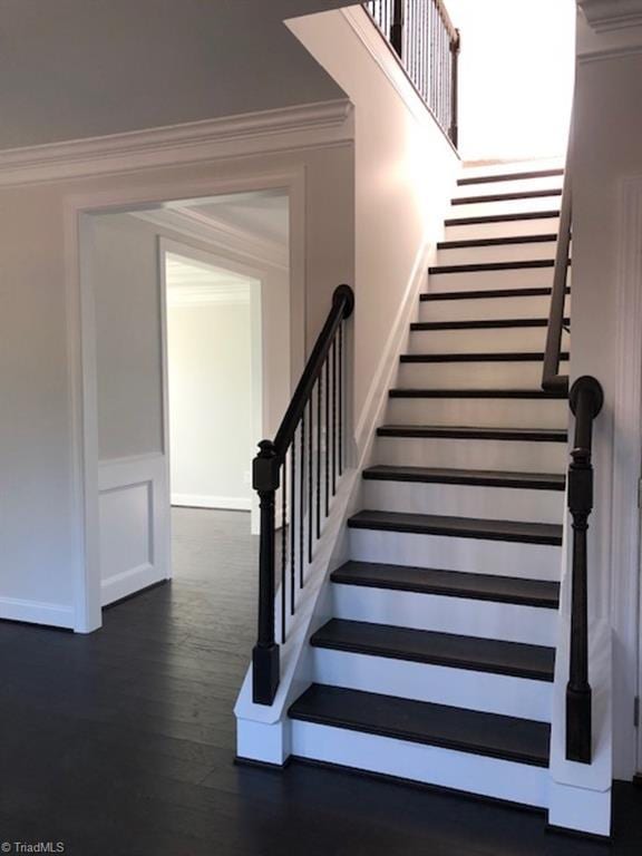 staircase featuring a decorative wall, wainscoting, ornamental molding, and wood finished floors