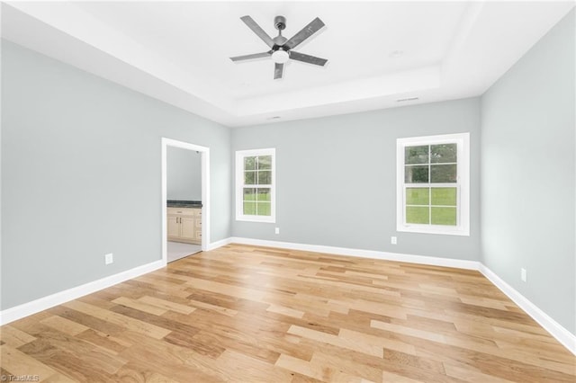 unfurnished room featuring a tray ceiling, light wood finished floors, ceiling fan, and baseboards
