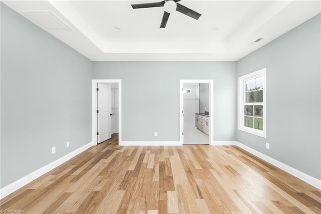 unfurnished bedroom with a tray ceiling, light wood-style floors, baseboards, and ceiling fan