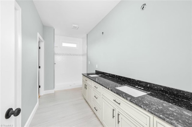 full bathroom featuring a shower, baseboards, and double vanity