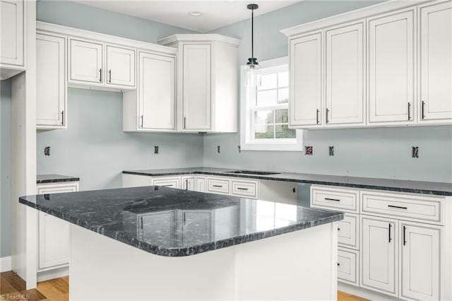 kitchen with dark stone counters, a center island, light wood-style flooring, hanging light fixtures, and white cabinets