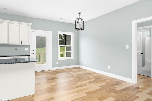 unfurnished dining area featuring light wood-style flooring, a chandelier, and baseboards