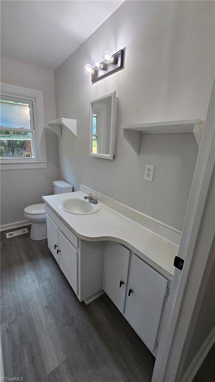 half bathroom with visible vents, toilet, vanity, and wood finished floors