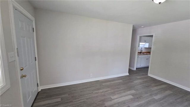 spare room with dark wood-style flooring, baseboards, and a sink