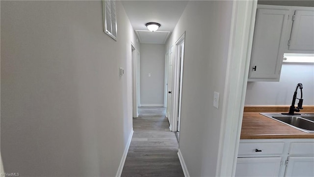 corridor with visible vents, wood finished floors, attic access, a sink, and baseboards