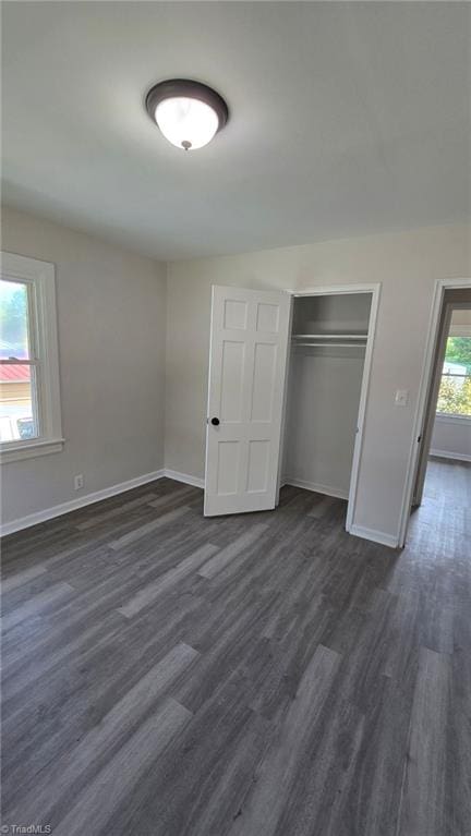 unfurnished bedroom with a closet, dark wood-style flooring, and baseboards