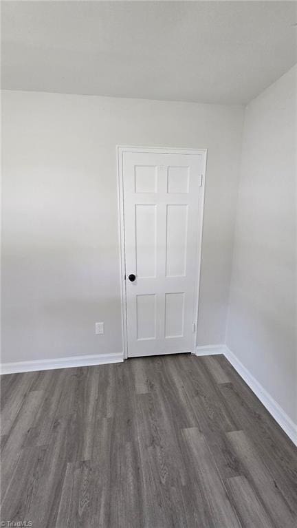 spare room with baseboards and dark wood finished floors