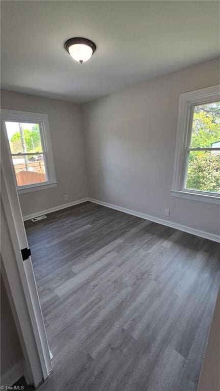 empty room featuring visible vents, dark wood-style flooring, baseboards, and plenty of natural light
