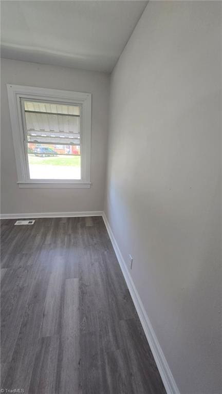 spare room with baseboards, dark wood-style floors, and visible vents