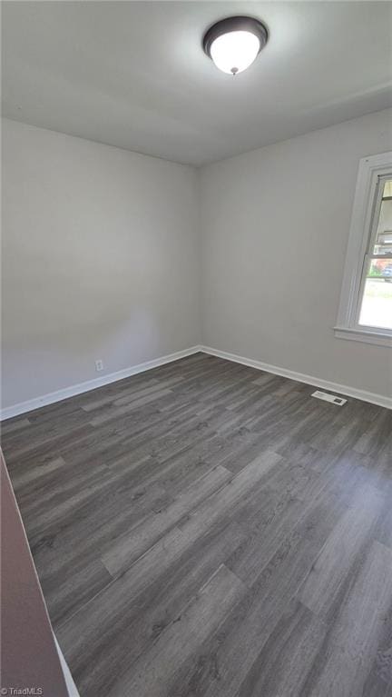 empty room featuring visible vents, baseboards, and dark wood finished floors