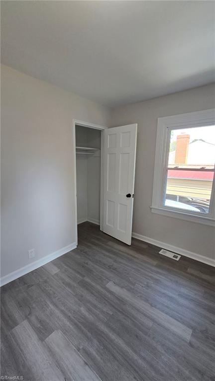 unfurnished bedroom featuring a closet, dark wood-style flooring, baseboards, and visible vents