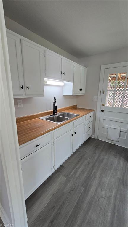 kitchen featuring white cabinets, butcher block countertops, a sink, and dark wood finished floors