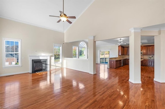 unfurnished living room featuring wood-type flooring, high vaulted ceiling, ceiling fan, and crown molding