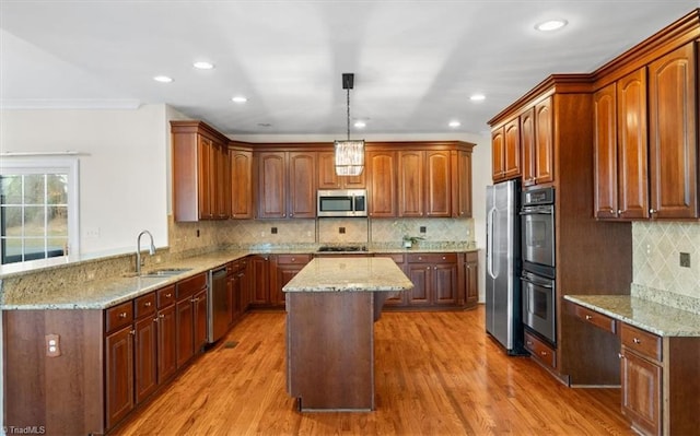 kitchen with sink, a center island, stainless steel appliances, decorative light fixtures, and light wood-type flooring