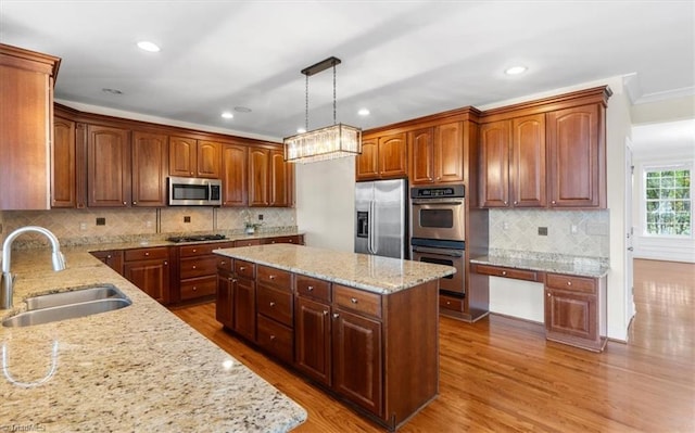 kitchen with appliances with stainless steel finishes, sink, pendant lighting, hardwood / wood-style flooring, and a center island