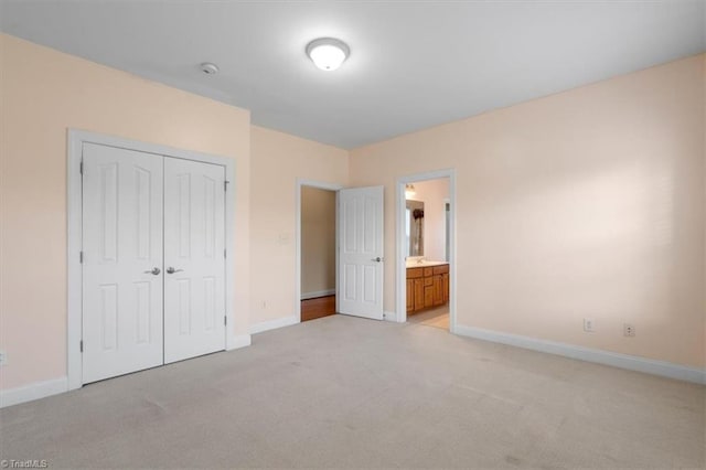 unfurnished bedroom featuring ensuite bath, light carpet, and a closet