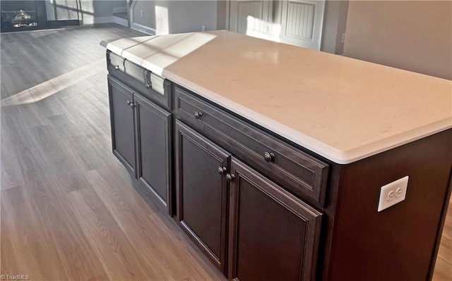 kitchen with a center island, dark brown cabinetry, open floor plan, light wood-type flooring, and light countertops