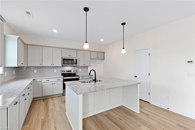 kitchen with a sink, light stone counters, tasteful backsplash, light wood-style floors, and appliances with stainless steel finishes