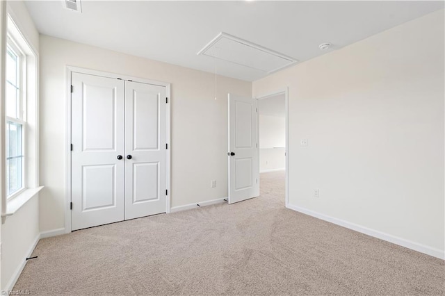 unfurnished bedroom with baseboards, multiple windows, light carpet, and attic access