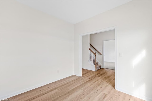 unfurnished room with baseboards, stairs, and light wood-style floors