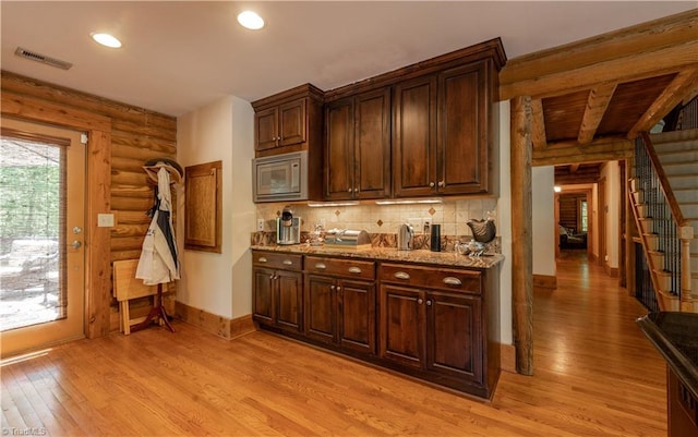 kitchen featuring log walls, light stone counters, tasteful backsplash, stainless steel microwave, and light wood-type flooring