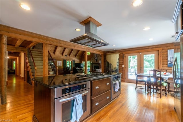 kitchen featuring island range hood, stainless steel appliances, light hardwood / wood-style flooring, french doors, and wooden walls