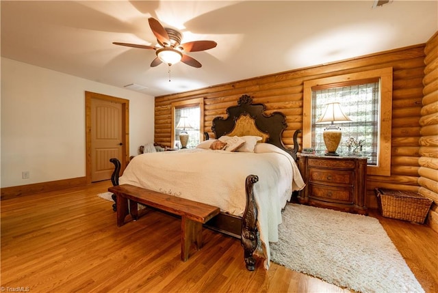 bedroom featuring light hardwood / wood-style floors, ceiling fan, and rustic walls