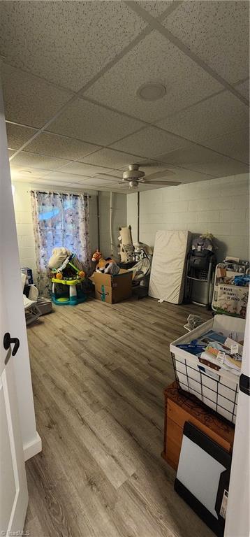 finished below grade area with a drop ceiling, wood finished floors, and concrete block wall