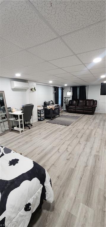 finished basement with a drop ceiling, wood finished floors, and a wall mounted AC